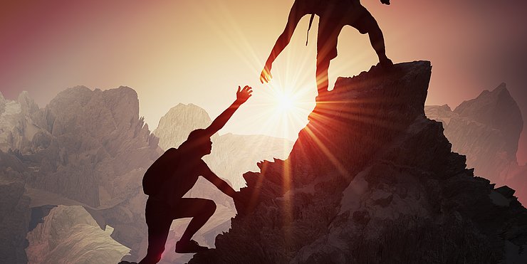 © Euregio uno scalatore sta per ragiungere la cima, il suo compagno dalla cima gli tende la mano